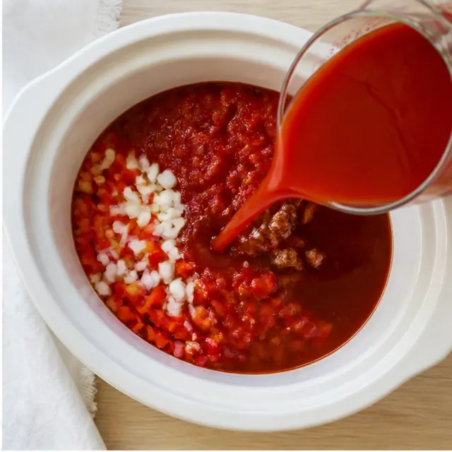 Pouring crushed tomatoes and broth into a slow cooker insert