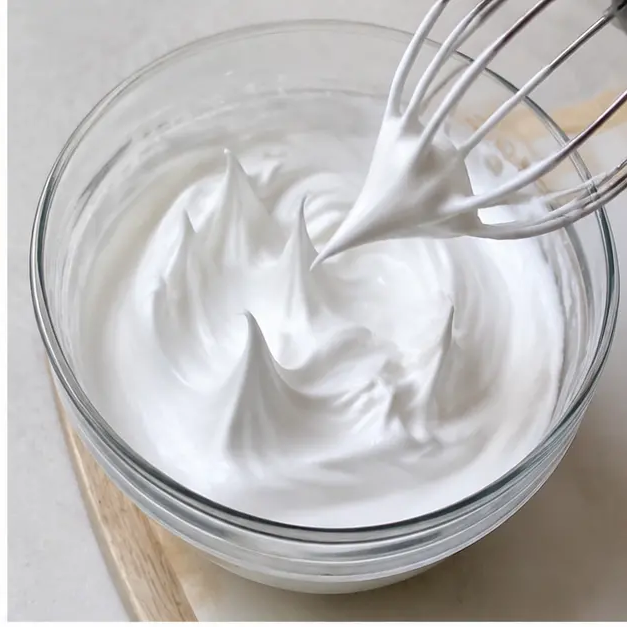 Adding sugar slowly to reach glossy stiff peaks