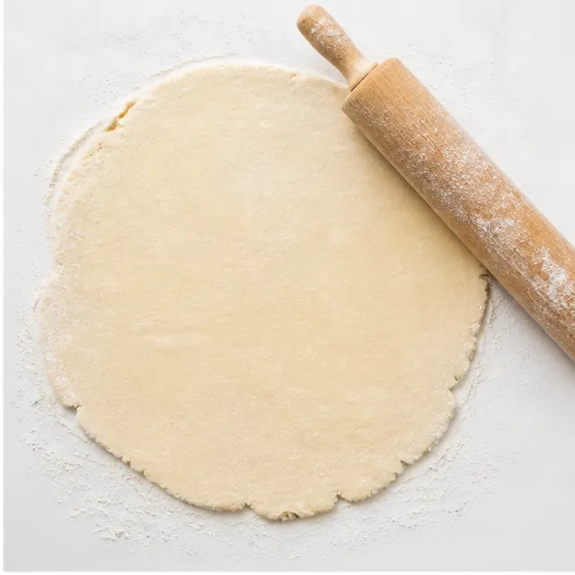 Rolling out the combined pie crusts into one large thin sheet on a floured surface